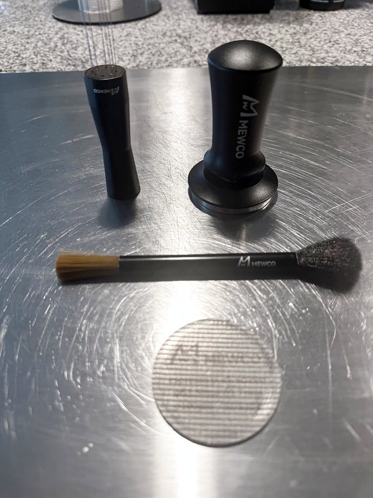 A MEWCO WDT tool, tamper, cleaning brush and puck screen laid out on a steel board
